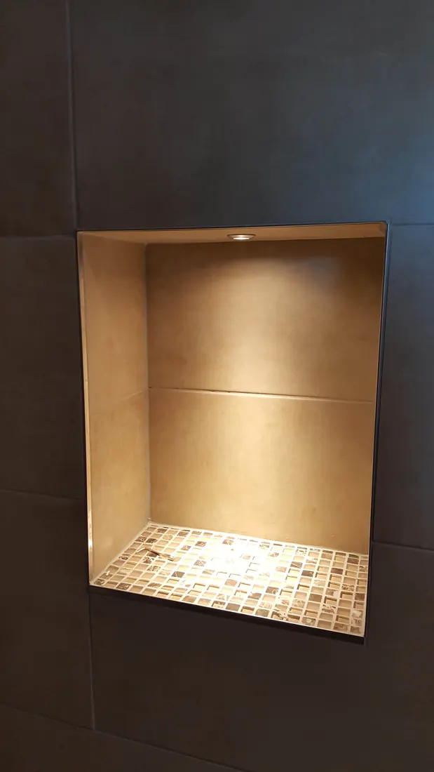 Beleuchtete Wandnische mit Mosaikfliesen in einer dunkel gefliesten Dusche